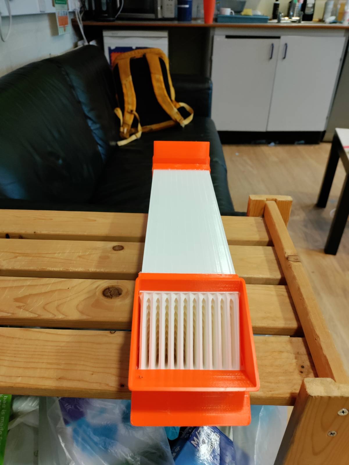 A white box section tube with orange end caps on a wooden bench, the diverter slots visible at the near end